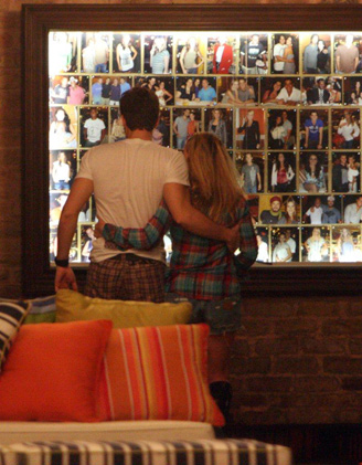 Abraçadinhos, Danielle e Jonatas conferem um painel de fotos no restaurante
