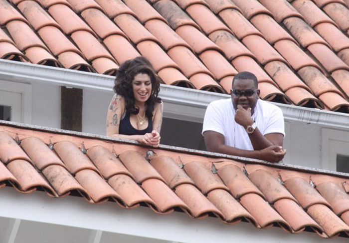 Amy Winehouse sai na sacada de hotel ao lado de segurança