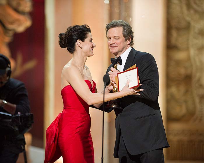 Colin Firth venceu como Melhor Ator pelo papel do monarca George VI em O Discurso do Rei e recebeu o prêmio das mãos de Sandra Bullock.