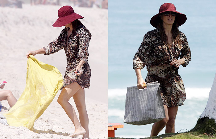 De chapéu e roupa, Christine Fernandes se bronzeia na praia