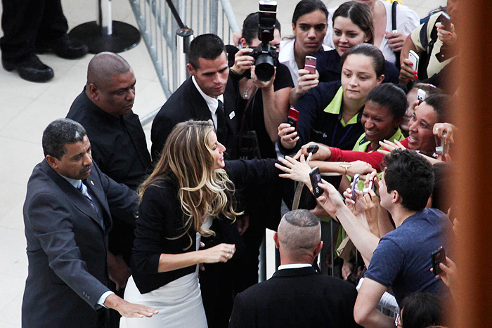 Ao sair do evento, cercada por seguranças, Gisele Bündchen dá atenção aos fãs.