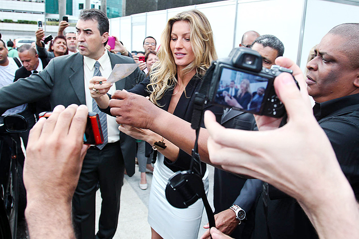 Ao sair do evento, cercada por seguranças, Gisele Bündchen dá atenção aos fãs.