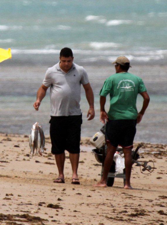 Ronaldo conversa com pescador enquanto segura um amarrado de peixes