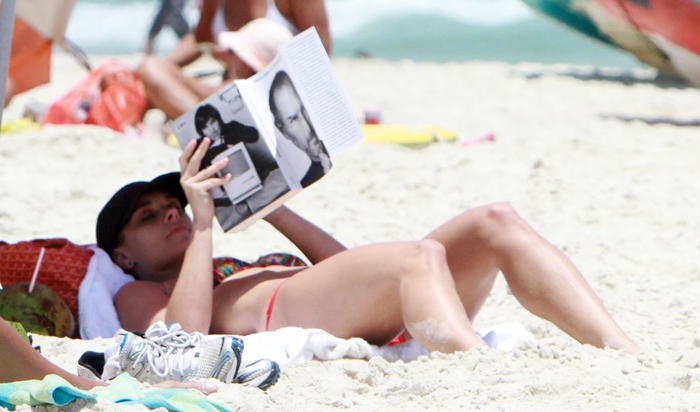Carolina Dieckmann relaxa na praia enquanto lê a biografia de Steve Jobs
