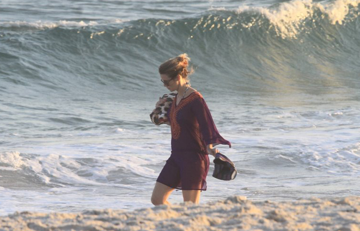 Sozinha e de roupa, Christine Fernandes caminha pela areia na Barra da Tijuca