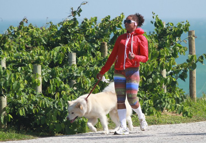 De jaqueta, Adriana Bombom passeia com cachorro pela praia