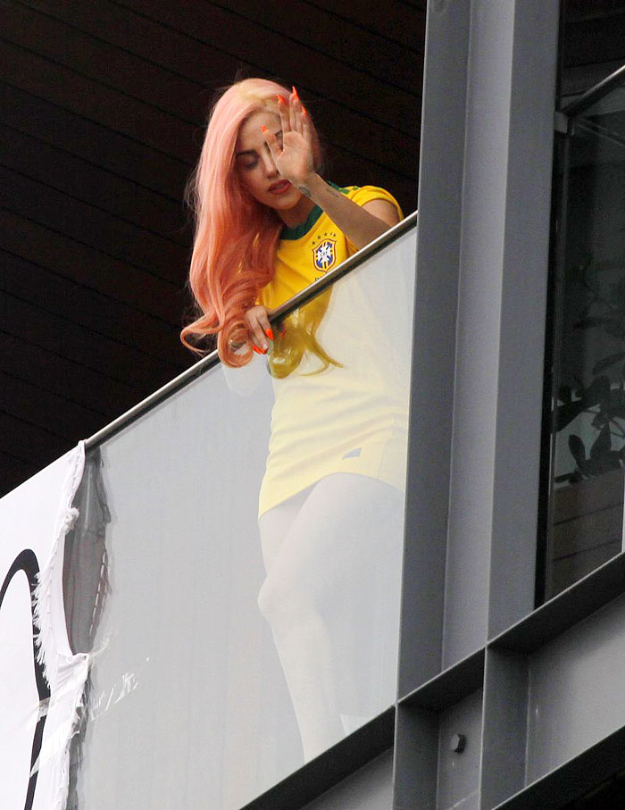 Lady Gaga aparece na sacada do hotel com cabelo rosa e camisa do Brasil