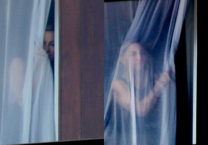 Madonna espia atrás da cortina da janela de hotel