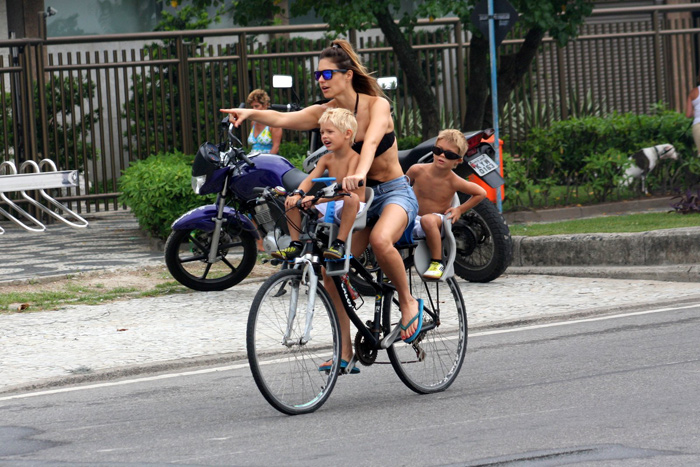 Fernanda Lima pedala com os gêmeos e vê celular ao mesmo tempo