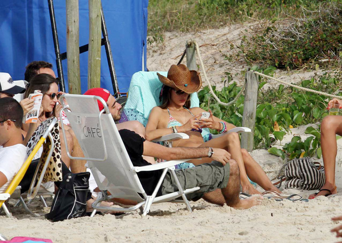 Alessandra Ambrósio não larga o celular em dia de praia