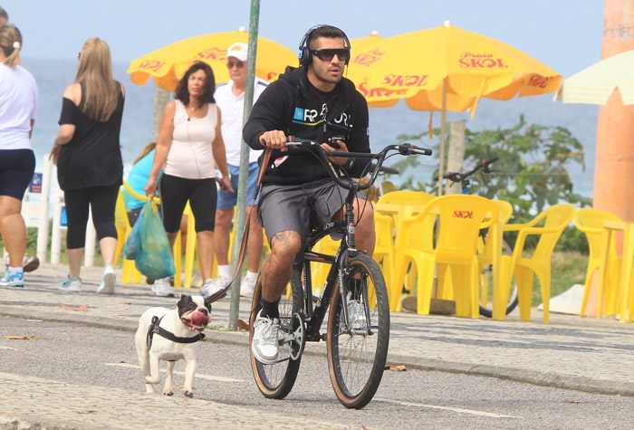 Ex-BBB Yuri pedala em companhia do seu cachorro em orla carioca