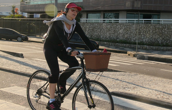 De boné e cachecol, Christiane Torloni pedala em orla carioca