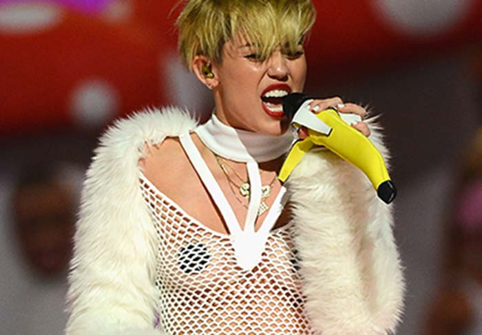 Miley Cyrus canta com seios à mostra, adesivo nos mamilos e microfone banana