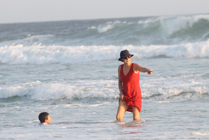 De vestido, Cássia Kis entra no mar com o filho