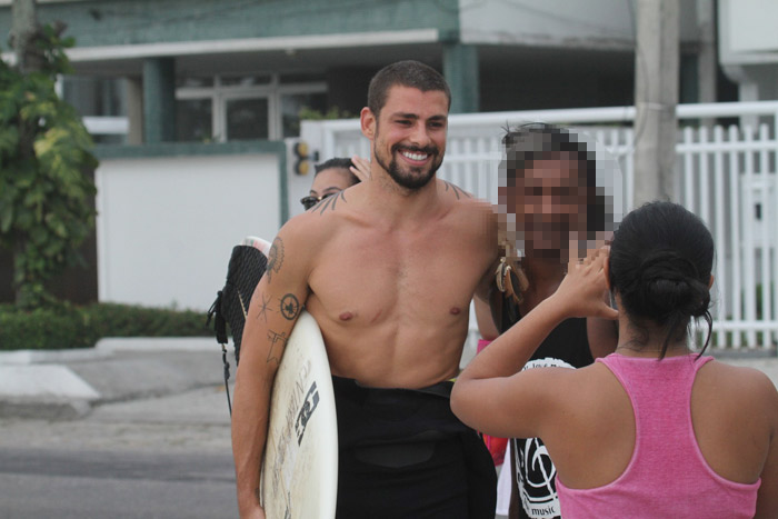 Cauã Reymond anda por orla com sorriso no rosto e prancha nas mãos