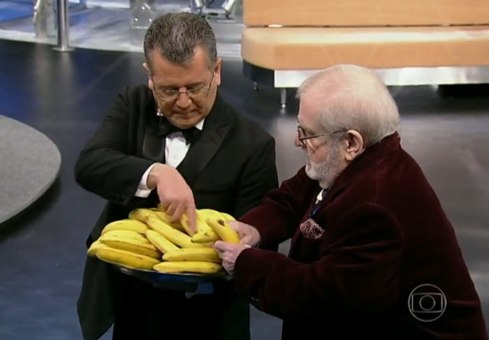 Jô leva um cacho de bananas e distribui para a plateia