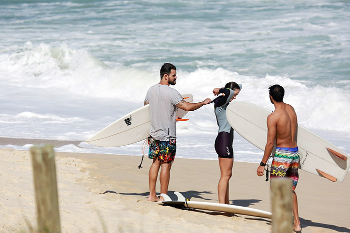 Juliano Cazarré ajuda a esposa a fechar a roupa de surf praia da Macumba, no Rio