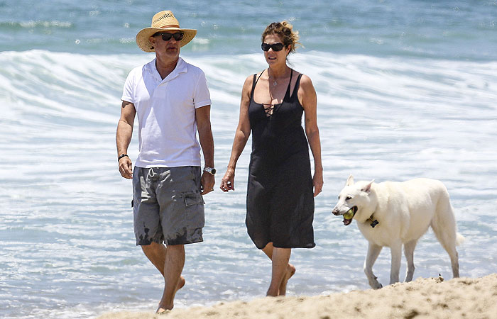 De chapéu, Tom Hanks passeia na praia com seu cachorro