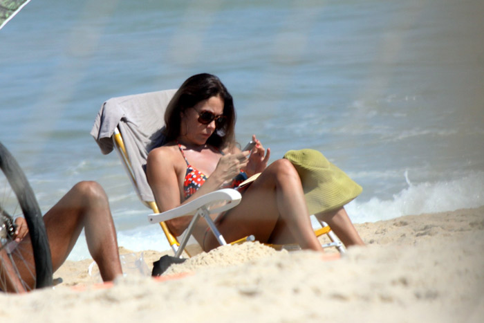 Carolina Ferraz lê jornal em tarde de praia com o namorado