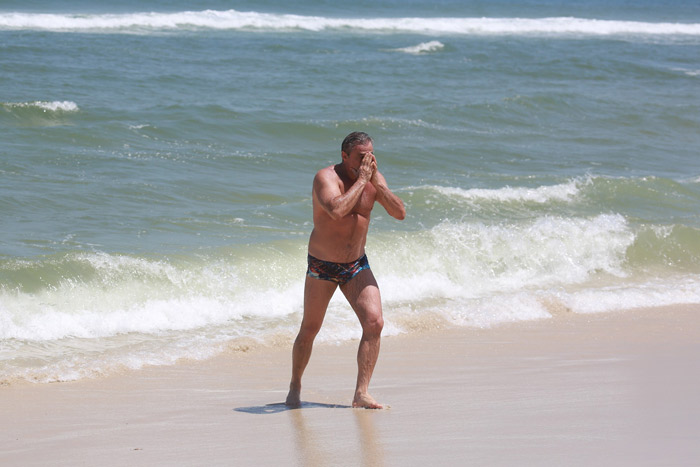 Oscar Magrini ajeita a sunga enquanto sai da praia na Barra da Tijuca