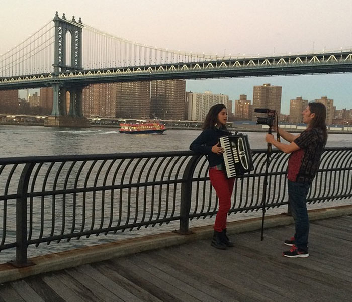 Lucy Alves toca sua sanfona arretada diante da Ponte do Brooklyn, em Nova York