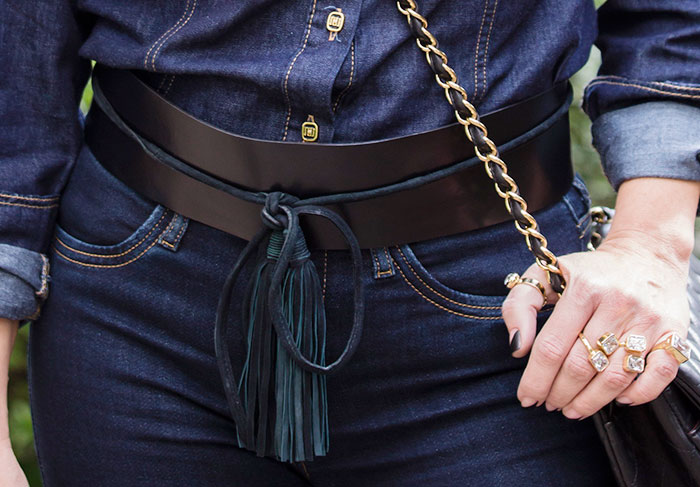 Detalhes do cinto em couro, conjunto de anéis triplo e botões da camisa jeans combinando com o tom dourado
