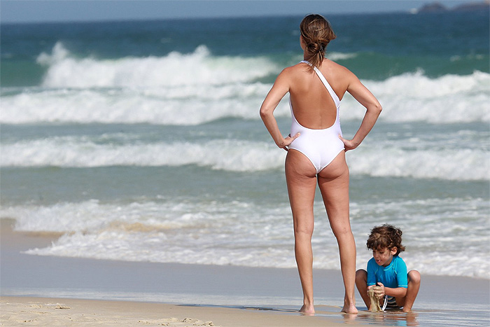 De maiô branco,  Letícia Birkheuer brinca com filho na praia