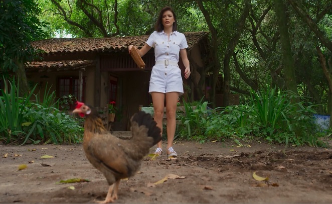Vitória Strada se divertindo com a galinha Felipa em cena de Salve-se Quem Puder, novela da Rede Globo