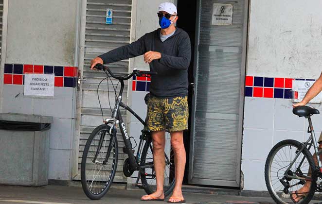 O look de Marcos Caruso para passear de bicicleta era máscara, blusa, um shorts e chinelos, além de boné