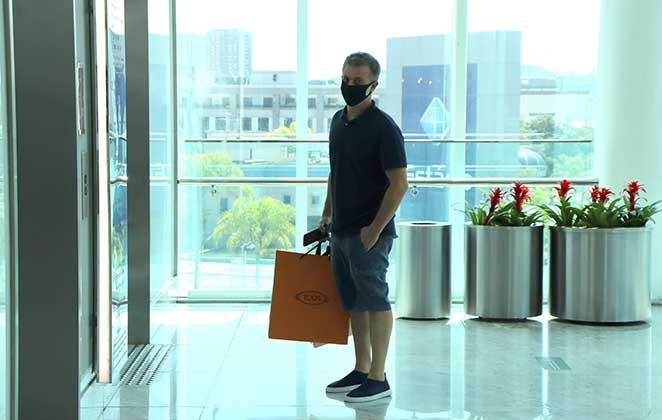 Luciano Huck com suas sacolas de compras aguardando o elevador