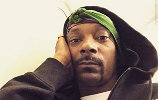 Close de Snoop Dogg, de lenço e touca, segurando o rosto