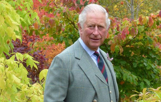 Príncipe Charles de terno e gravata em um jardim