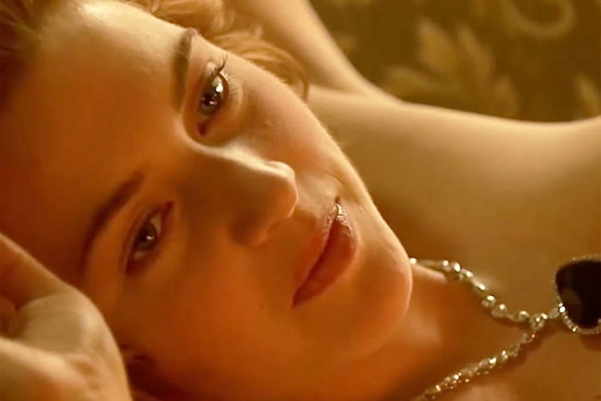 Kate Winslet deitada usando apenas um colar de pérolas