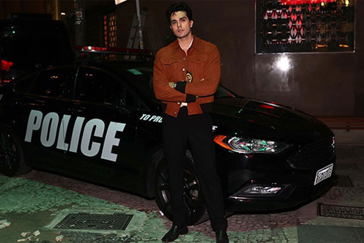 Luan Santana encosta no carro de polícia em clipe