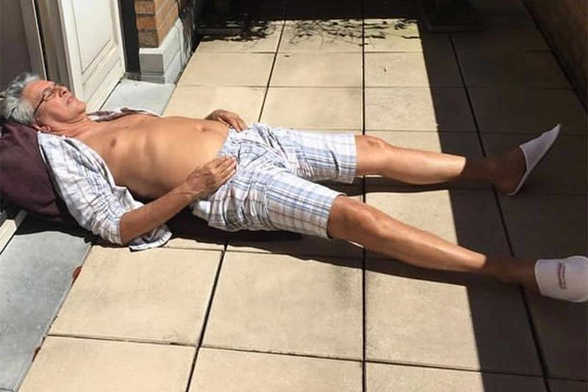 Caetano Veloso deitado, tomando sol na varanda, de camisa aberta