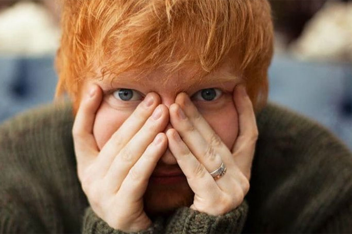 Ed Sheeran com as mãos no rosto, olhando para a câmera