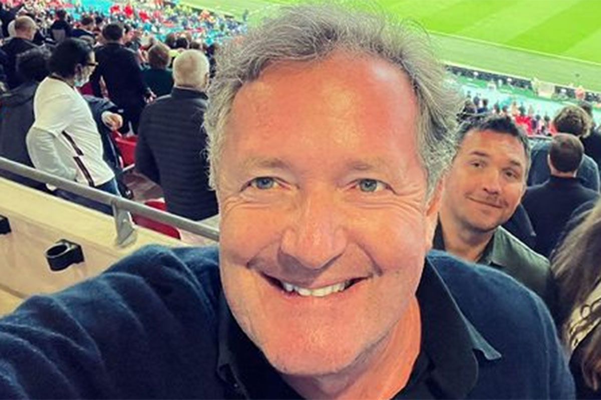 Piers Morgam sorridente, em arquibancada de jogo de futebol
