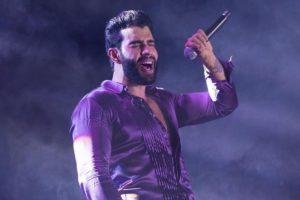 Gusttavo Lima cantando em show, com o figurino e a iluminação roxa