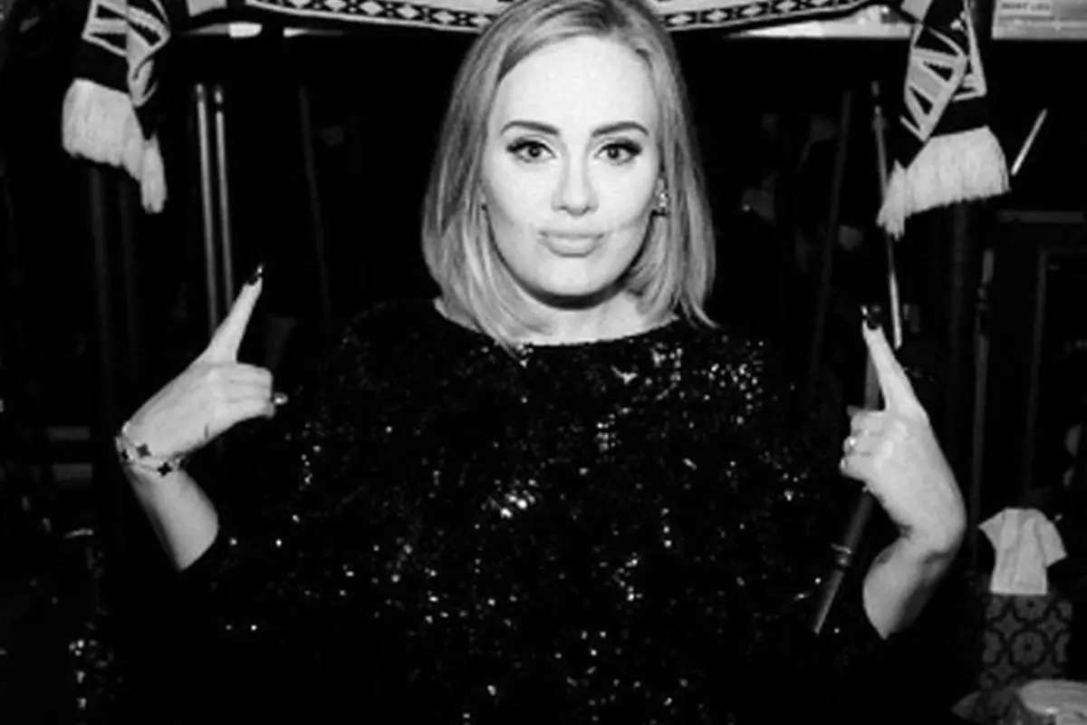 adele em foto preta e branca sorrindo levemente e apontando para cima