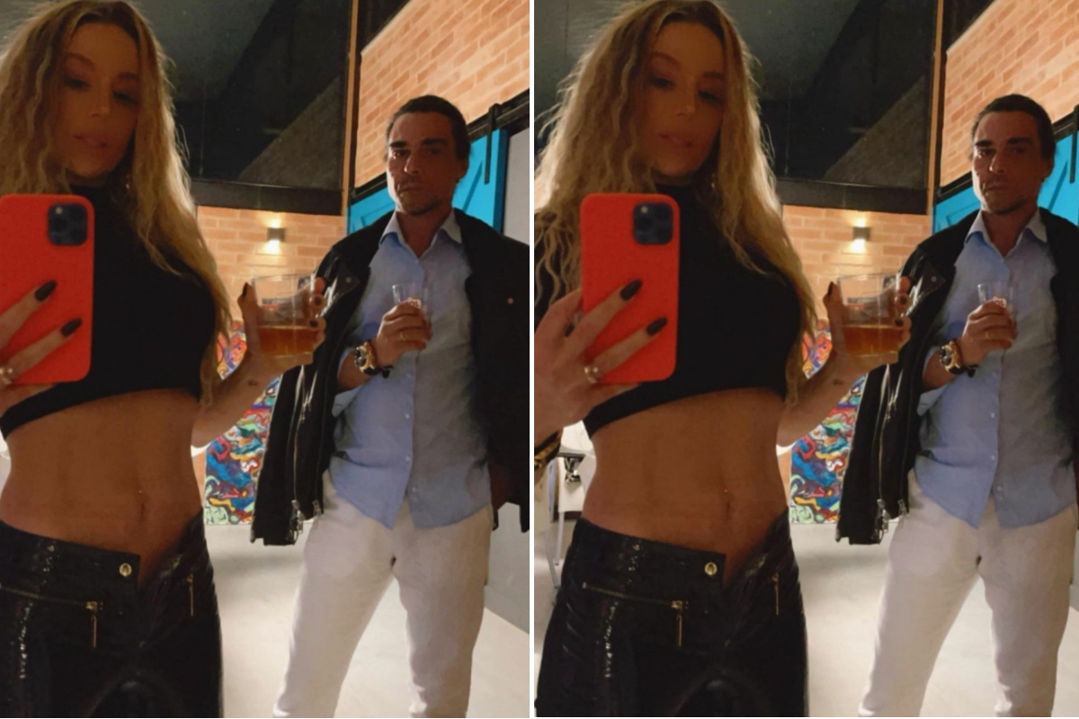 Danielle Winits faz selfie de barriga de fora e mostra André Gonçalves ao fundo