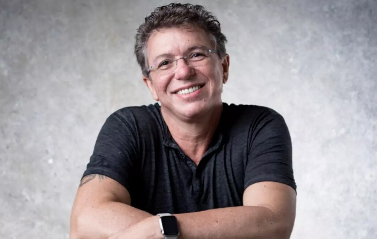 Boninho sorrindo, de braços cruzados, camisa preta