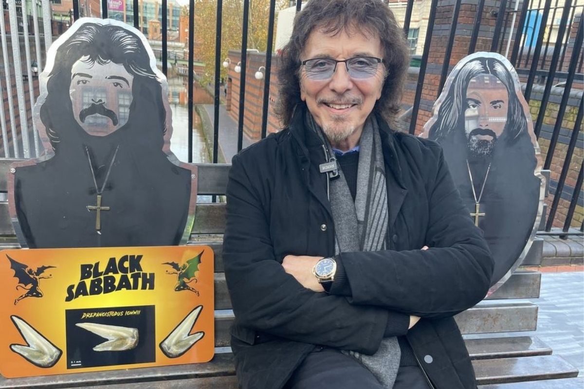 Tommy Iommi em foto com o logo do Black Sabbath ao lado