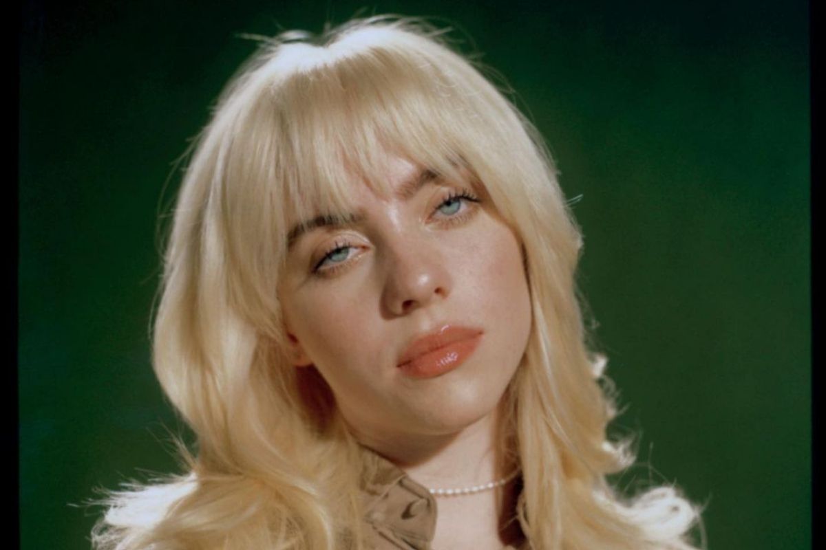 Billie Eilish em retrato com o cabelo loiro, curto, um fundo vende e semblante sereno