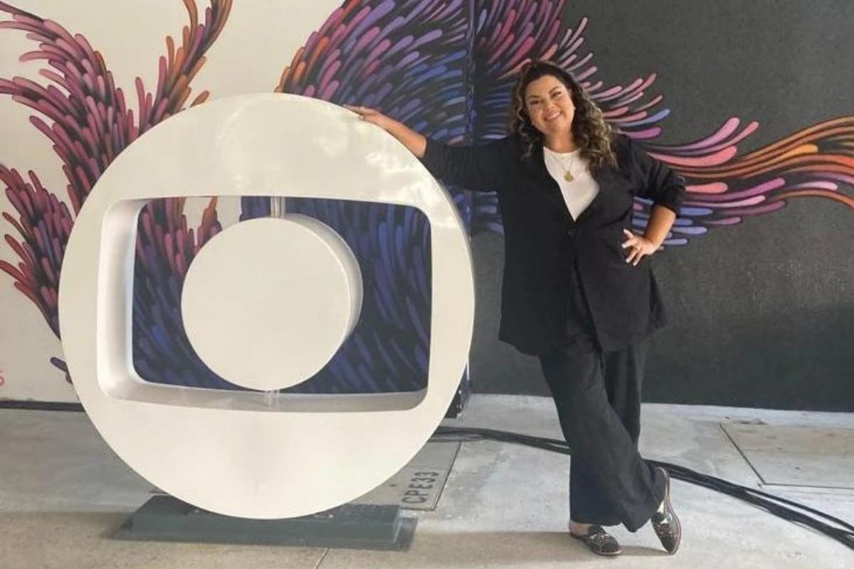 Fabiana Karla posando para foto ao lado do logo da TV Globo