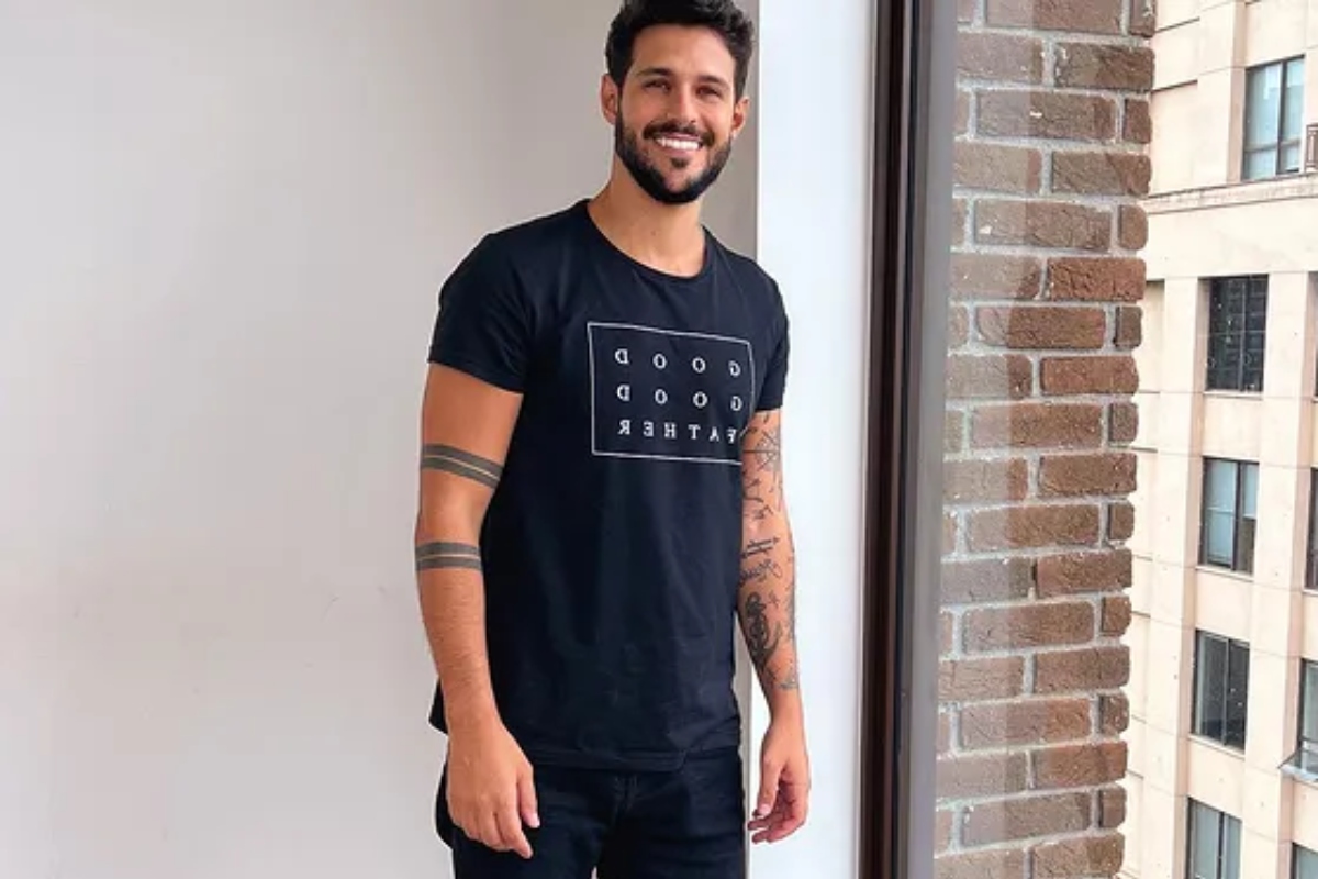 rodrigo mussi posando sorridente com camiseta preta em novo apartamento