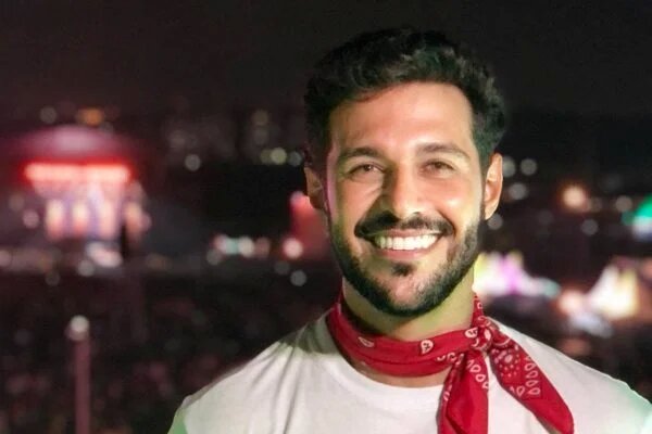 Rodrigo Mussi sorrindo, de bandana no pescoço e camisa branca
