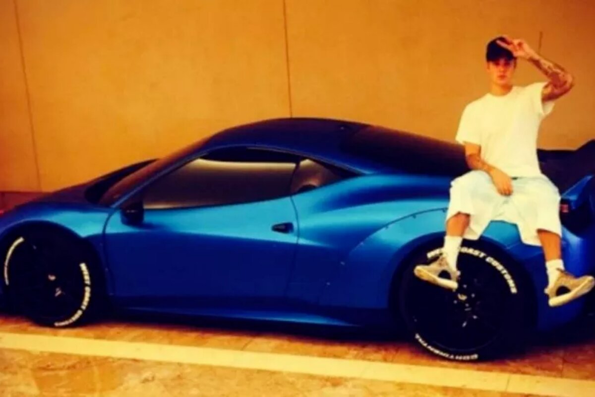 Justin Bieber encostado em uma Ferrari azul