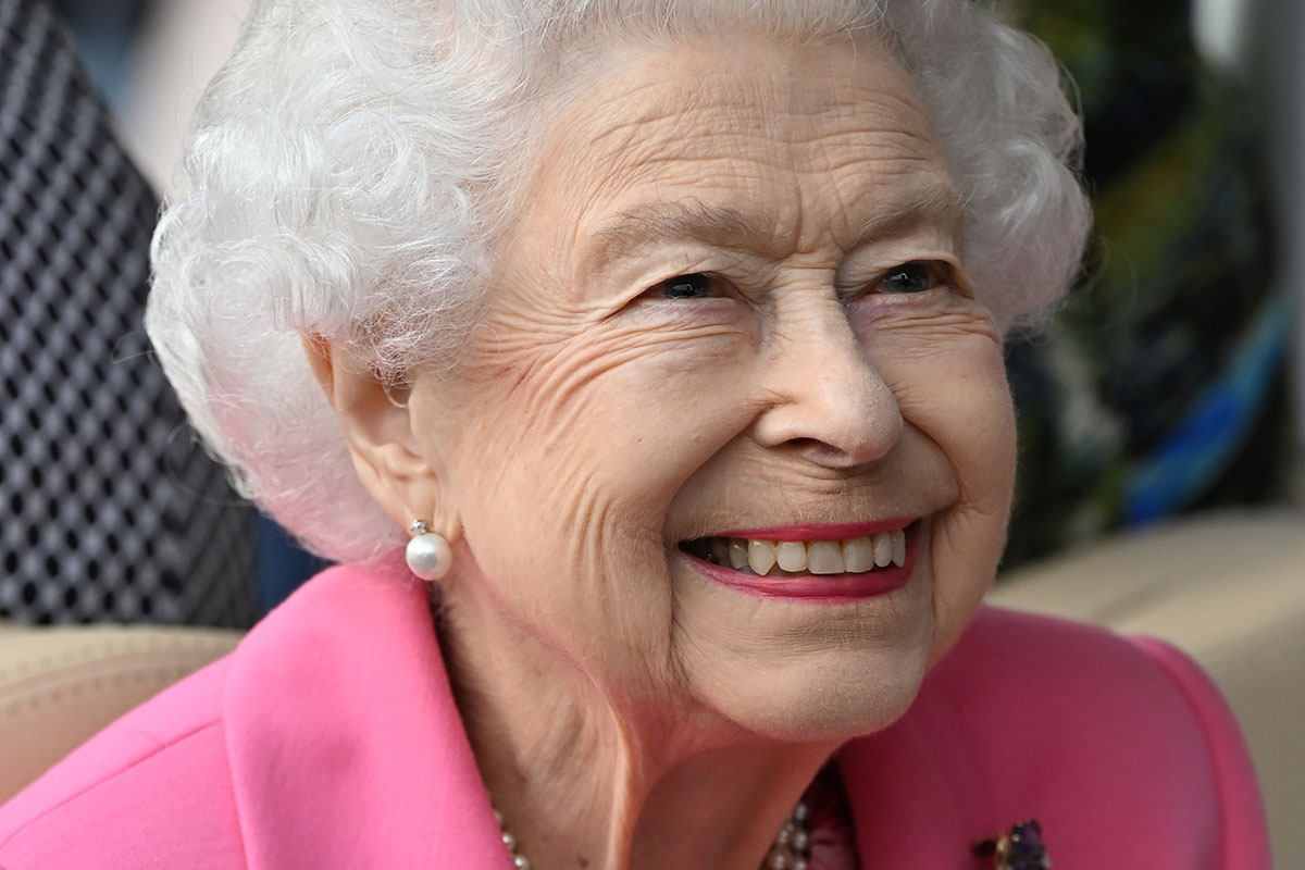 Rainha Elizabeth, com brincos de pérola, roupa rosa e sorridente