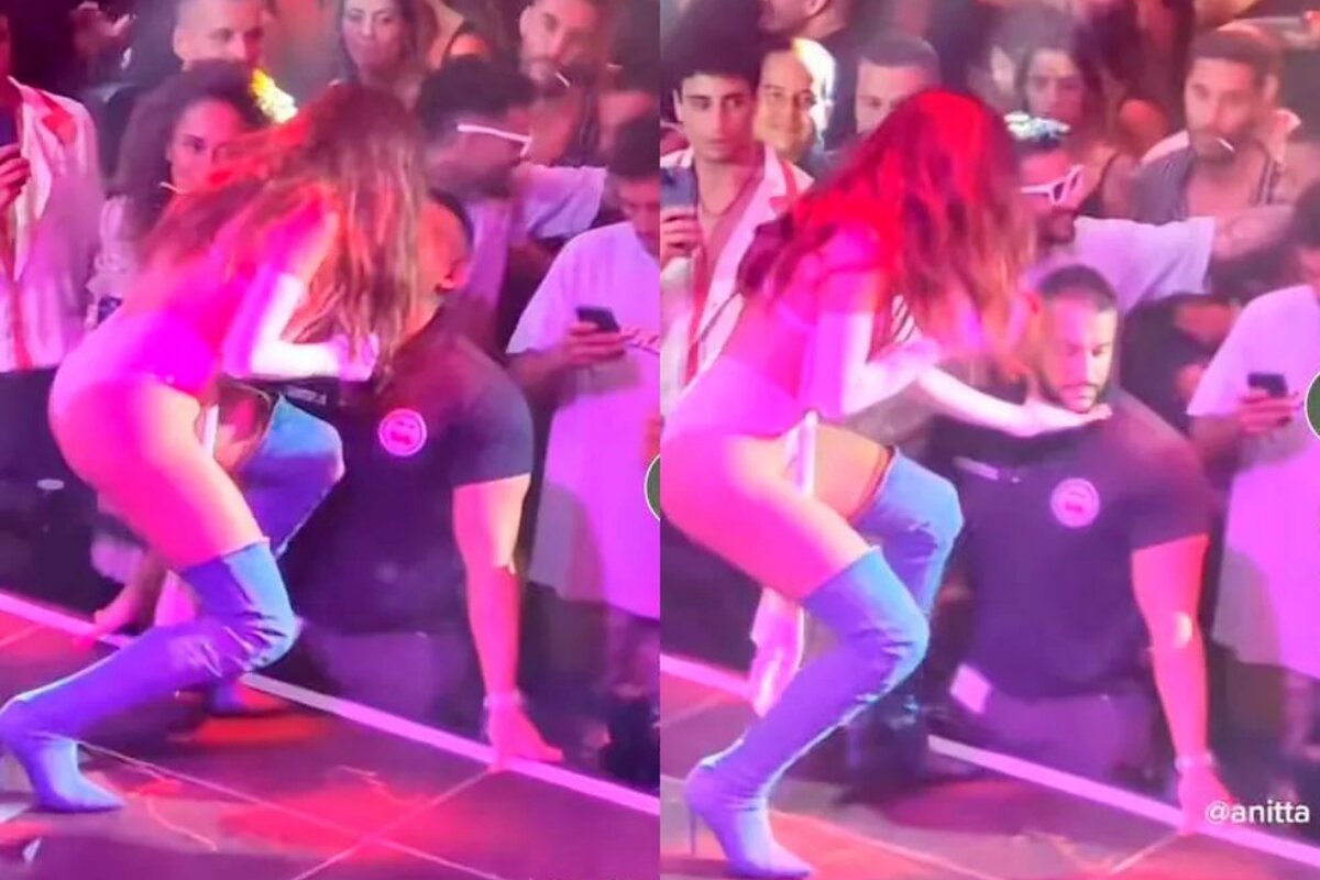 Anitta no palco, de botas azuis longas, supostamente beijando segurança durante show