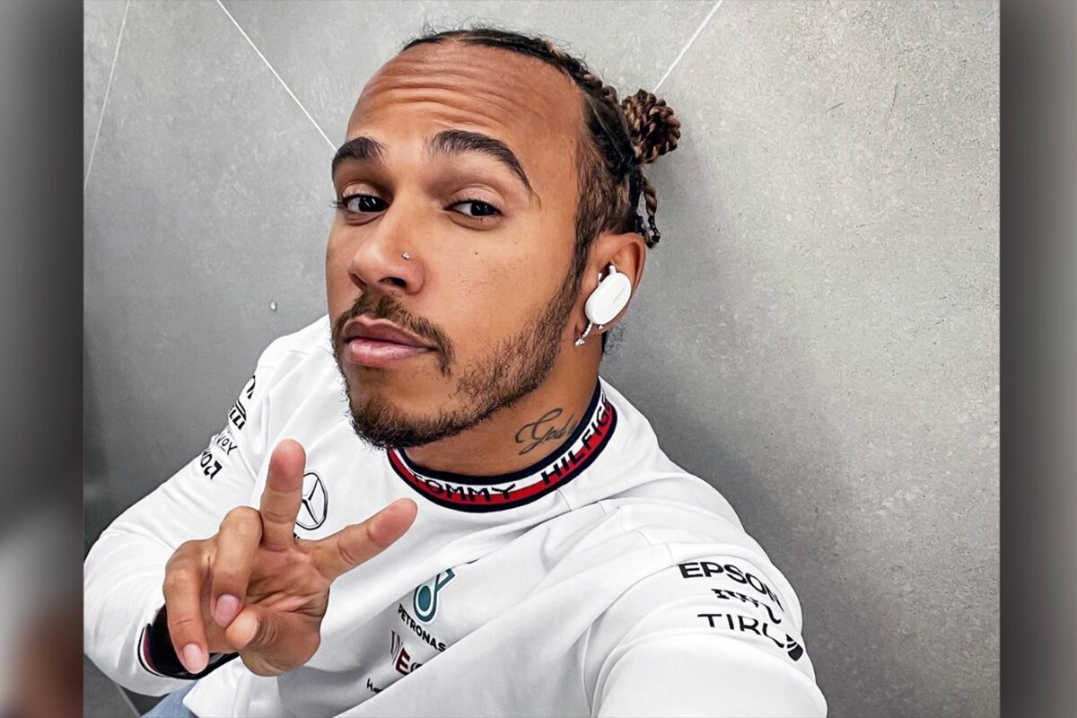 Lewis Hamilton e macacão branco, fazendo selfie com sinal de positivo